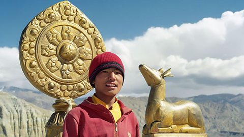 A Buddhist young man stands in front of a Dharma Wheel.