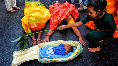 Hindu women in prayer at the side of a baby - A Hindu girl holds a branch with leaves on over the baby.