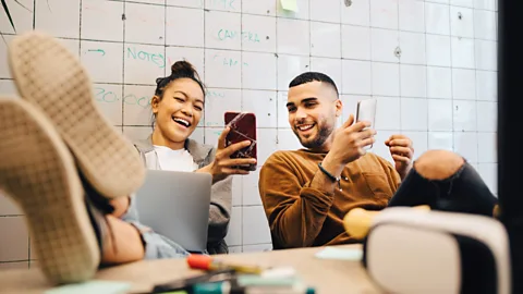 Two young workers looking at their phones