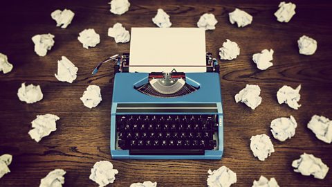 A type-writer on a table with several pieces of paper scrunched up around it representing writer's block.