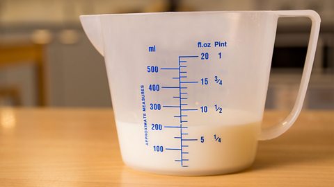 A white plastic measuring on a surface with 200 milliltres of milk inside the jug