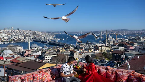A couple pose for a photo at rooftop towards city view as daily life continues in Istanbul, Turkiye on December 26, 2023. Tourists exploring Istanbul capture souvenir photos against the backdrop of the cityscape on the historical peninsula (Credit: Getty)