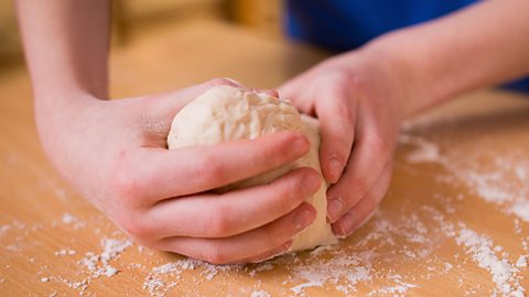 A child's hands grabbing the dough and turning it around