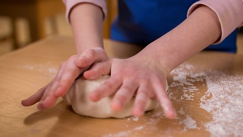 Close up of a child's hands pressing some dough on a work top