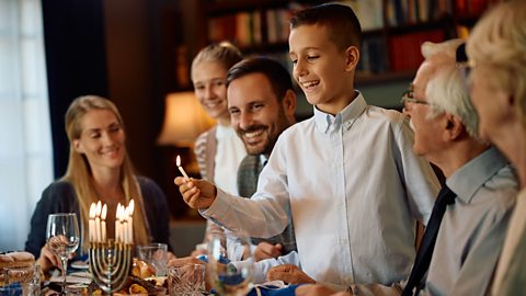 A Jewish boy lighting the menorah during family meal