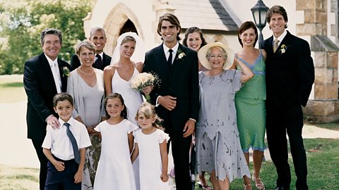 An extended family posing for a wedding photo outside of a church. The newly wedded couple stand in the middle.