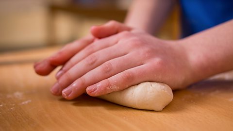 A child's hands rolling out dough on a work top