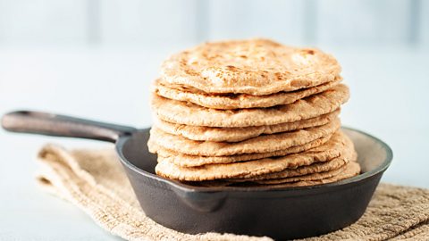 A stack of flat chapatis in a metal pan