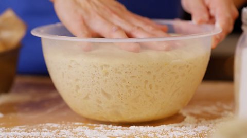 A hand pressing down on risen dough in a bowl