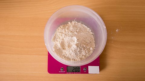 A set of pink scales from above showing 200 grams on the display, with a bowl of flour on top of the scales