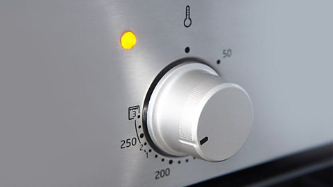 A close up of an oven temperature dial at 250 and an orange light.