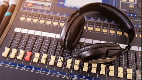 Headphones rest on a sound mixing desk. The bottom of the mixing desk is filled with sliding switches ready to move up and down.