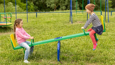 Two young girls on a seesaw in a park.