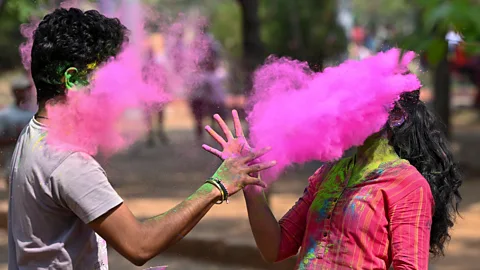 Two people throw pink powder at each other during Holi