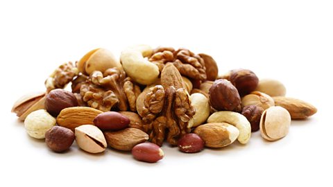 Mixed nuts including walnuts, pistachios, almonds and hazelnuts in a pile on a white background