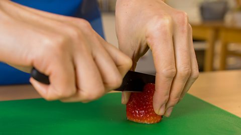 A woman's hands cutting a strawberry in half on a green chopping board