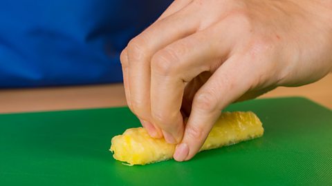 A woman's hand gripping a section of pineapple on a green chopping board.