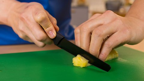 A woman's hands holding a black paring knife and cutting into a pineapple