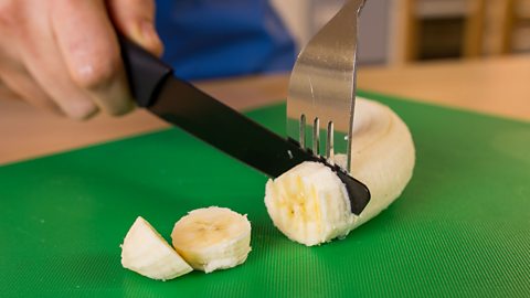 A banana being sliced using the fork secure method