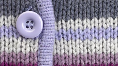 A close up of a purple button attached to knitted fabric