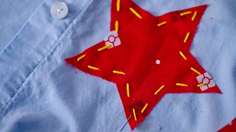 A close up of a red fabric star attached to a blue shirt by a yellow running stitch