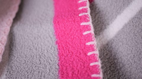 A close up of a line of white stitches forming a continuous line around the edge of a wool blanket