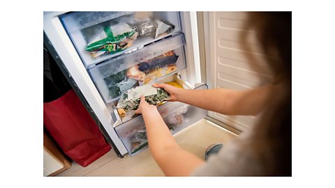 A woman taking out a bag of frozen vegetables from the bottom drawer of a freezer