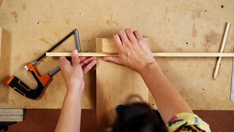 A thin piece of wood is pushed up against the backrest of a bench hook.