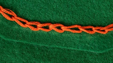 a row of orange chain stitches on some green fabric