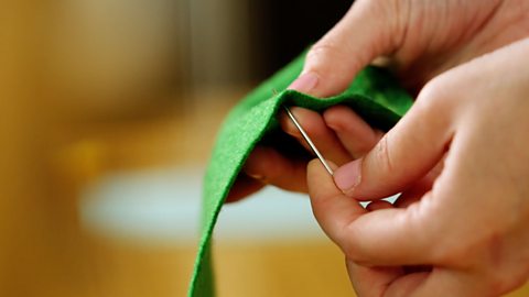 A pair of hands holding green fabric and pushing a needle up through the back of the fabric