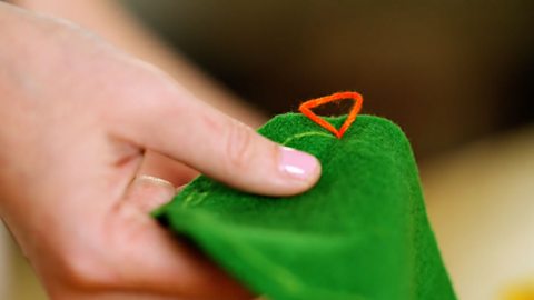 A pair of hands holding green fabric and a loop of red thread