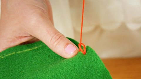 A pair of hands holding green fabric and pulling red thread through a loop