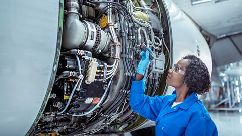 A woman holding a torch up to an open aircraft jet engine