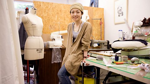 A fashion designer perched on a table. A mannequin and design equipment