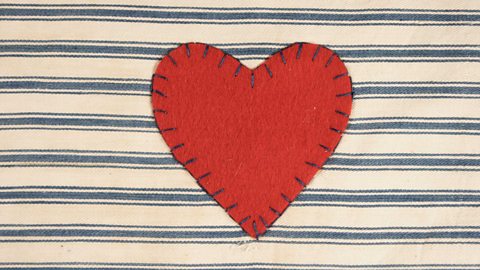 A red heart appliqué patch sewn onto blue and white striped material with an overstitch