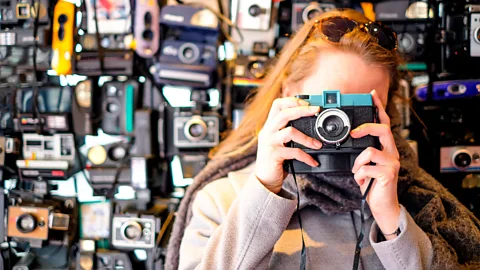 Woman using film camera with shelves of film cameras behind (Credit: Getty Images)