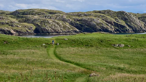 A woman with a backpack wanders across the green meadows of Handa Island (Credit: Getty Images)