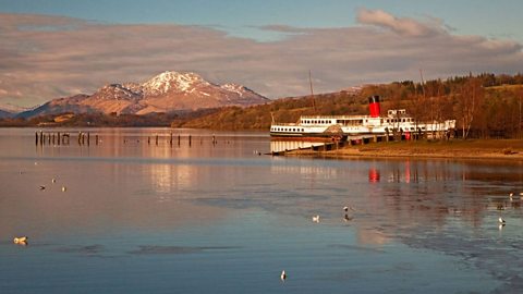 Sealladh de Loch Laomainn bho chladach a' Bhealach. Tha bàta agus beinn le mullach sneachda air a' chùl.