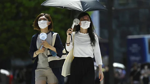 Women in protective Covid-19 masks cool themselves with fans in Tokyo, July 2022 (Credit: Getty Images)