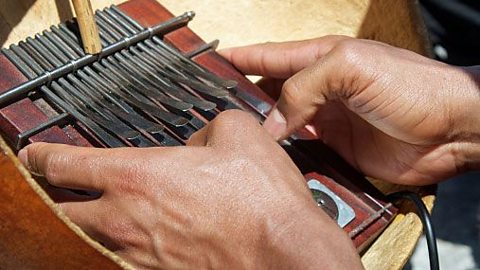 An instrument being held by two hands with the thumbs positioned over wooden bars which can be flicked.