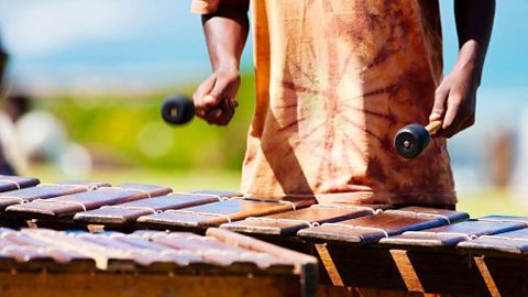 A person holding two beaters playing an instrument with large wooden bars.  