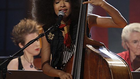 A female bass player performing on stage and singing into a microphone.