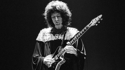 A black and white photograph of a male musician playing an electric guitar.