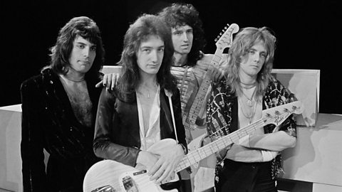 A black and white photo of four male musicians in a casual group pose.  Two are holding electric guitars.