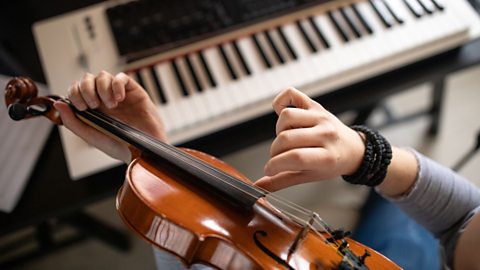 A view from above of a violin being held in a person's left hand and the strings are being plucked by the right hand.