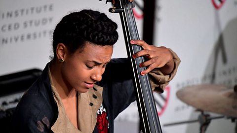 A close up photo of a female musician playing a double bass at a performance.