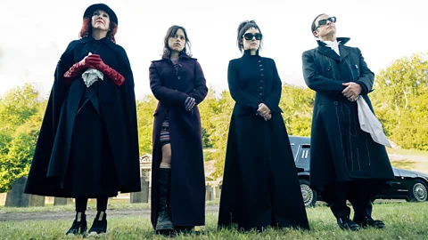 A still from Beetlejuice of four figures in black standing with trees and sky in background (Credit: Warner Bros/ Parisa Taghizadeh)