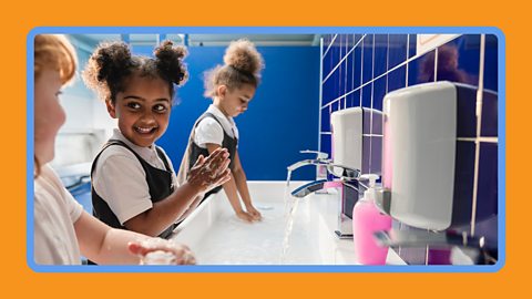Three young children at school washing their hands with soap.