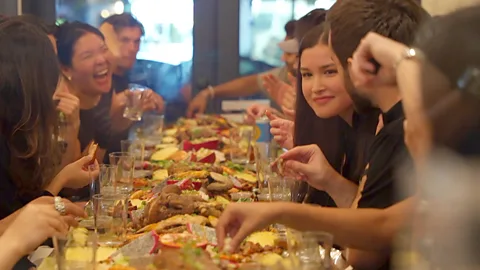 A party sit around a table with a Filipino kamayan feast (Credit: Darryl Laiu/ BBC)