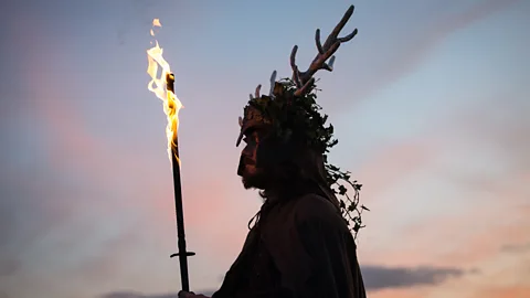 A man celebrating Samhain. He is silhouetted, carrying a flaming torch and wearing a headdress (Credit: Getty Images)